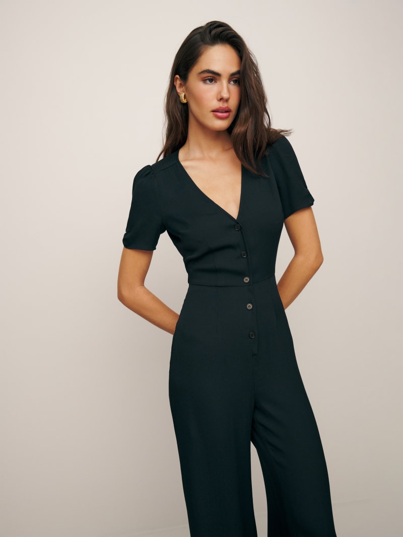 A woman wearing a black Petites France jumpsuit with a V-neck, button-down front, and wide-leg pants.