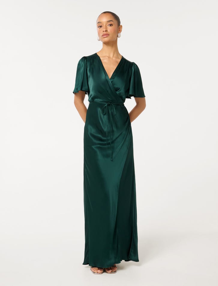 A woman wearing a long, emerald green satin maxi dress with flutter sleeves, a V-neckline, and a tie at the waist.