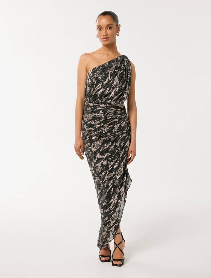 A woman wearing a black and beige one-shoulder midi dress with an abstract pattern, paired with black high-heeled sandals.
