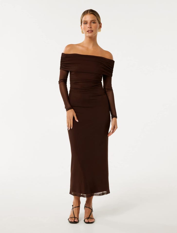 A woman wearing a brown off-shoulder midi dress with ruched detailing and sheer long sleeves, paired with black strappy heels.
