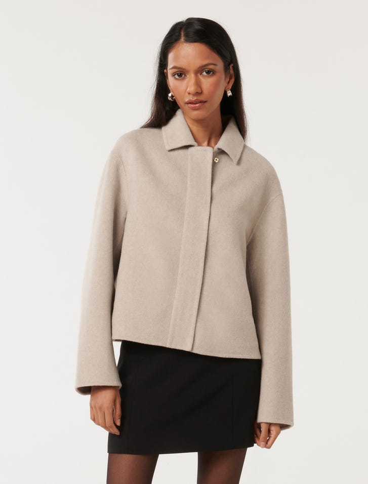 A woman wearing a beige zip front felled jacket with a collar, long sleeves, and a relaxed fit, paired with a black skirt.