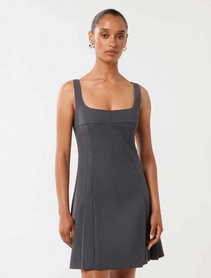 A woman wearing a dark grey sleeveless pleated mini dress with a square neckline and fitted bodice.