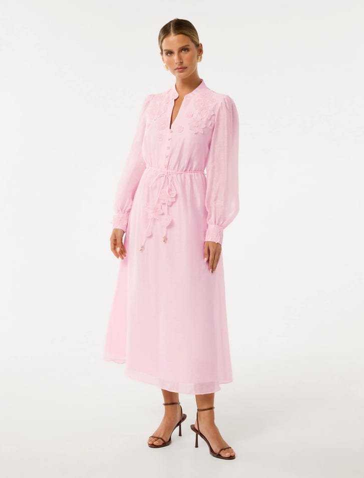 A woman wearing a pink floral detail midi dress with long sleeves and a V-neckline, paired with high-heeled sandals.