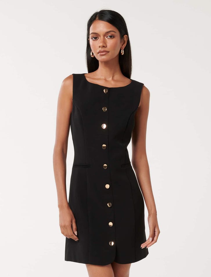 A woman wearing a black sleeveless mini dress with gold buttons down the front, round neckline, and fitted style.