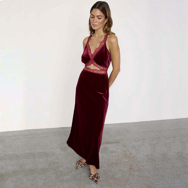 A woman wearing a burgundy velvet dress with lace details on the straps and bust, standing against a plain background.