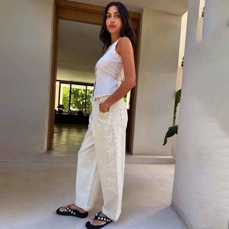 A woman wearing ecru petite barrel jeans with silver studded detailing along the seams, paired with a sleeveless top and black sandals.