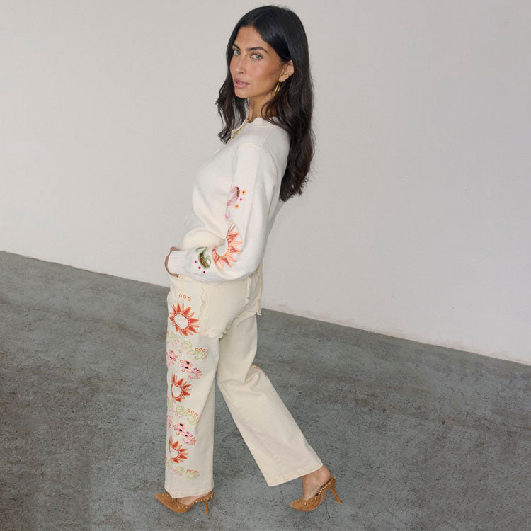 A woman wearing Ecru Enchanted Cut Work Scallop Jeans Petite, which are structured denim with embroidered motifs, scalloped pockets, and a wide-leg fit.