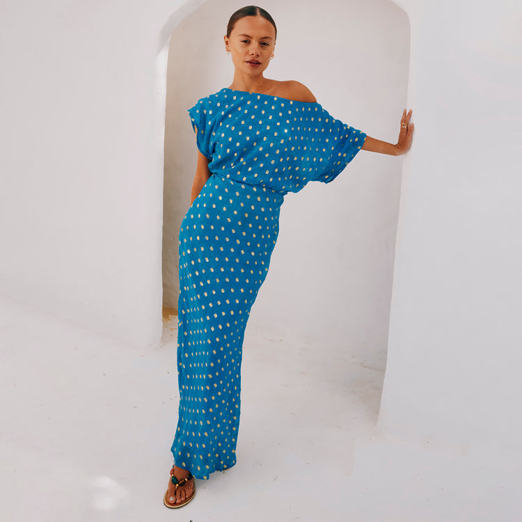 A woman wearing a blue jacquard Tilly dress petite with a gold fleck print, asymmetric off-the-shoulder neckline, fitted skirt, and voluminous top.
