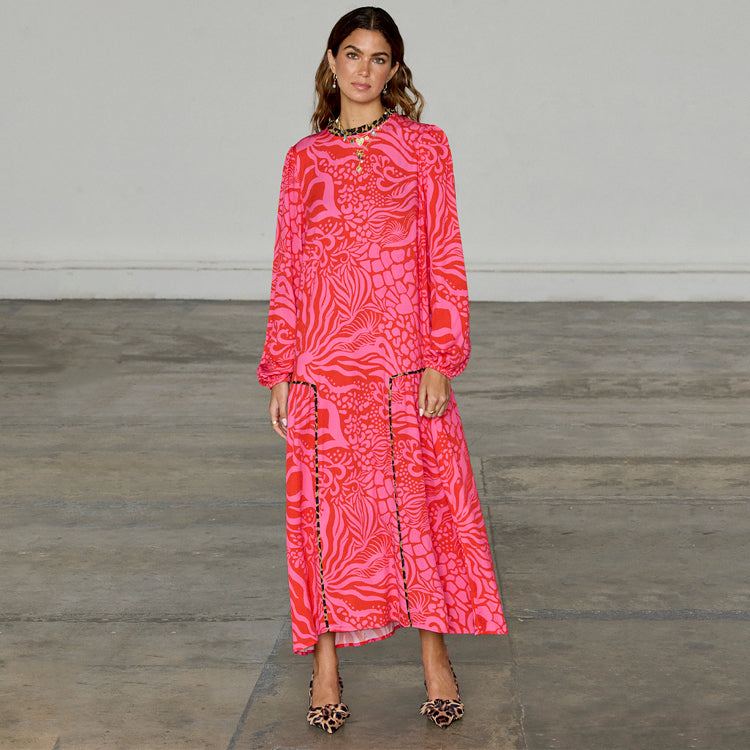 A woman wearing a pink and red floral print dress with leopard details on the skirt and neckline, long blouson sleeves, and leopard print heels.