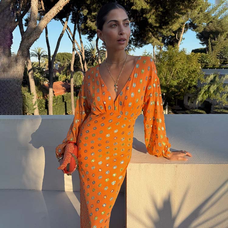 A woman wearing an orange dress with multicoloured foil circle print, elasticated sleeves, and a V-neckline, standing outdoors.