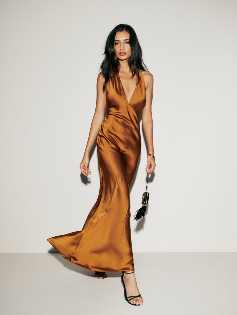 A woman wearing a copper-brown satin Petites Daniela Silk Dress with a halter neckline and open back, paired with black high-heeled sandals.