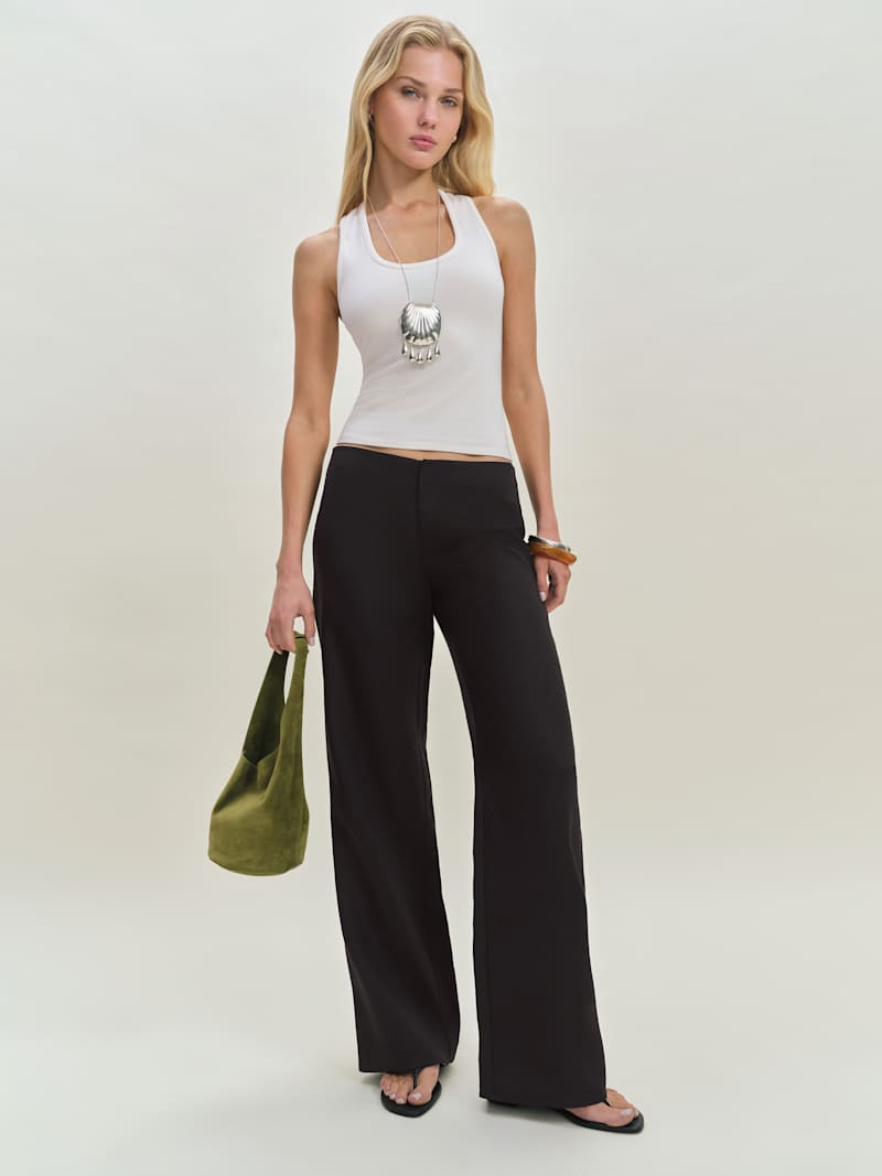 A woman wearing beige linen low-rise pants with a relaxed fit and wide-leg style, paired with a white tank top and accessories.