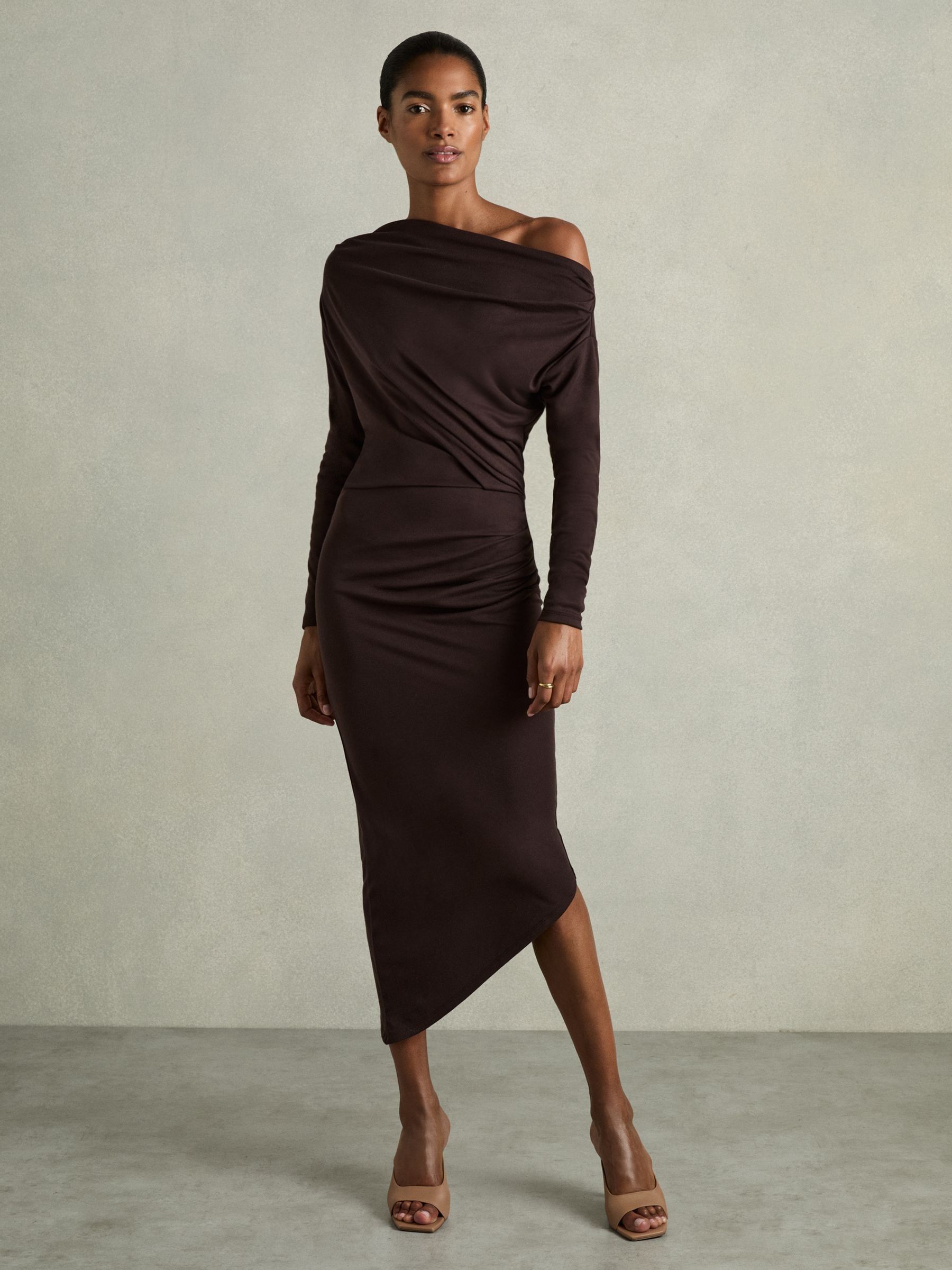 A woman wearing a brown off-the-shoulder jersey midi dress with ruched details and asymmetric hem.