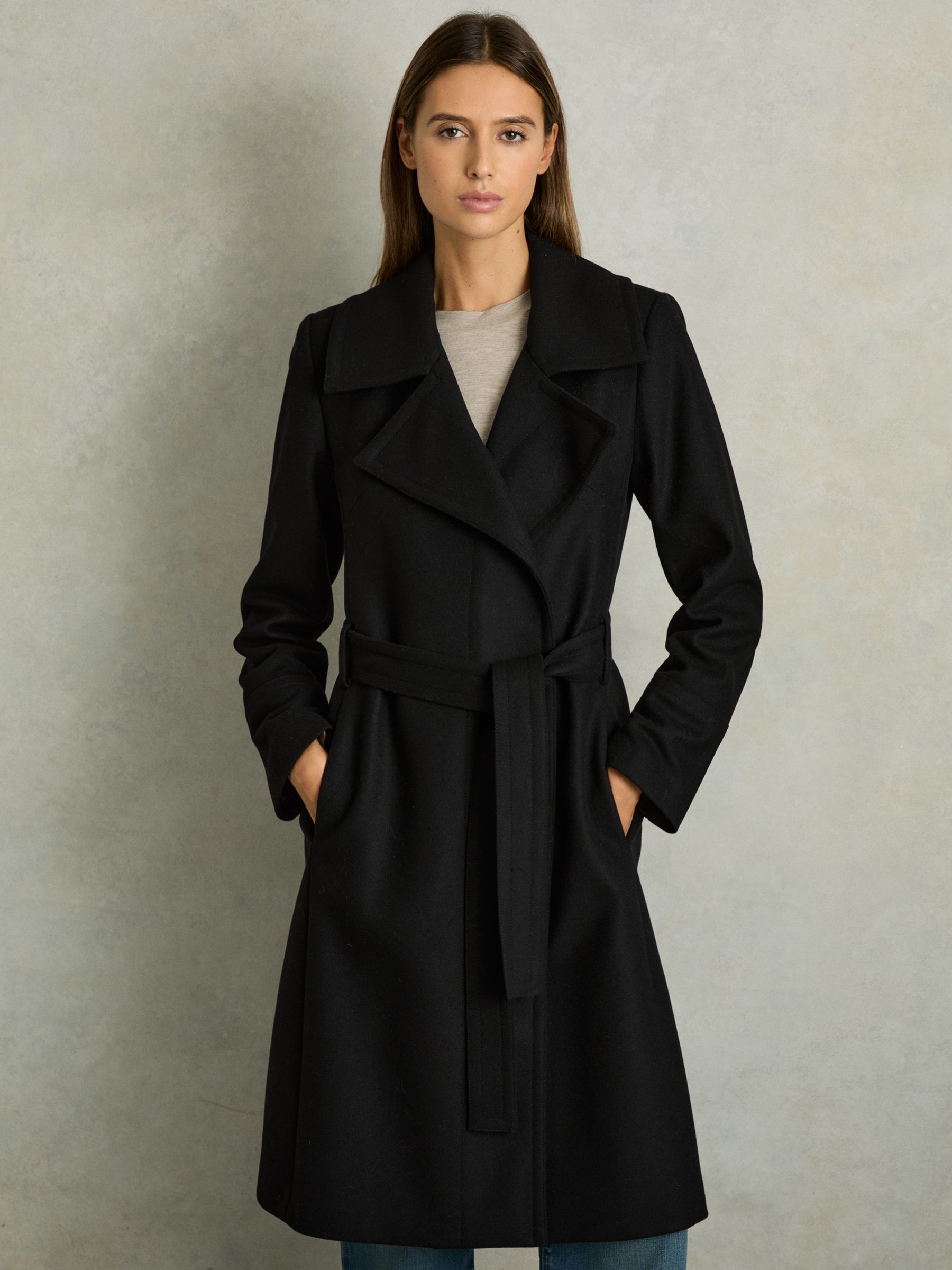 A woman wearing a black wool blend belted double-breasted coat with a notched collar and knee-length hem.