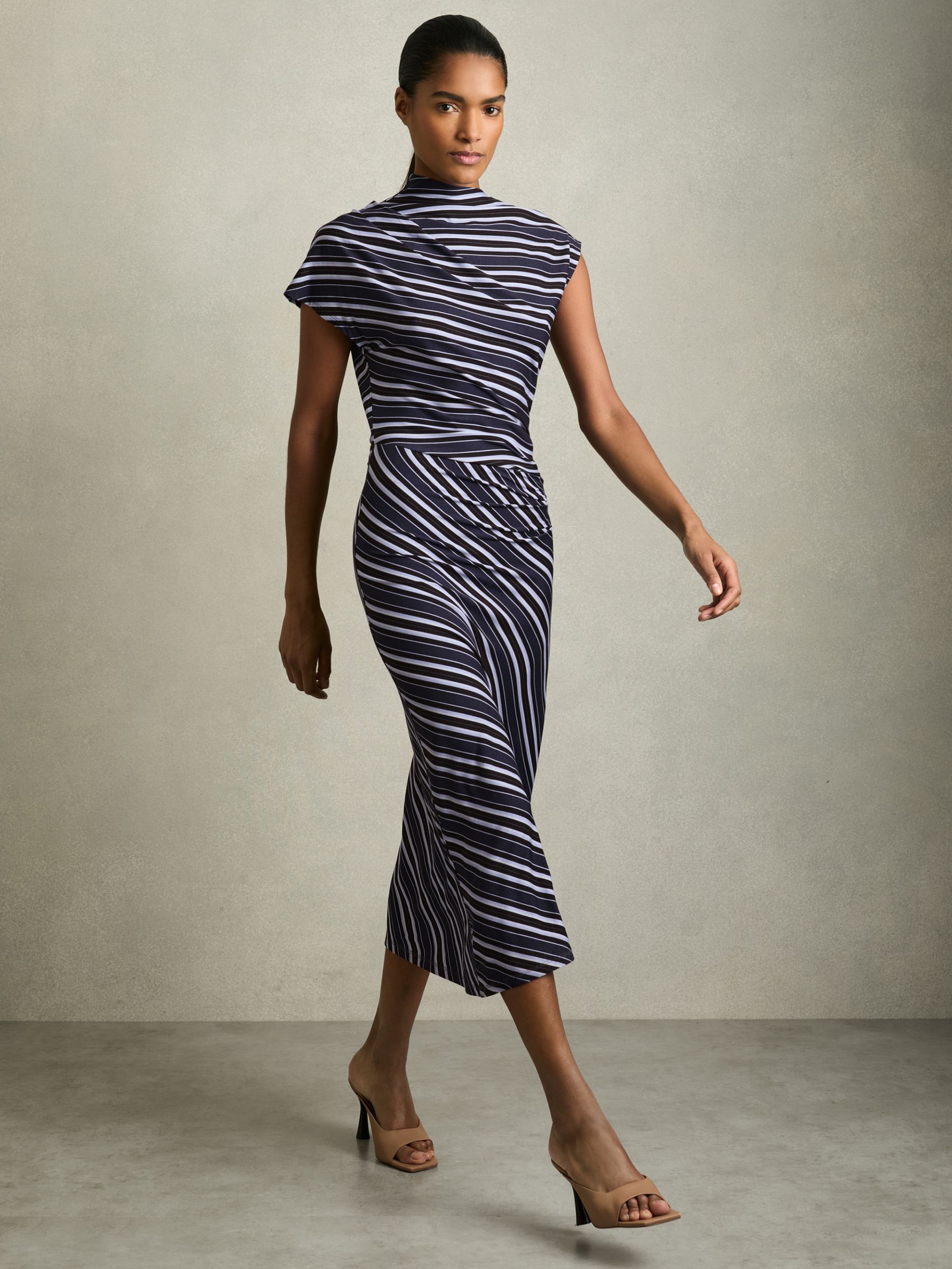 A woman wearing a blue stripe-print draped midi dress with a high neckline, asymmetric design, and stretch jersey fabric.