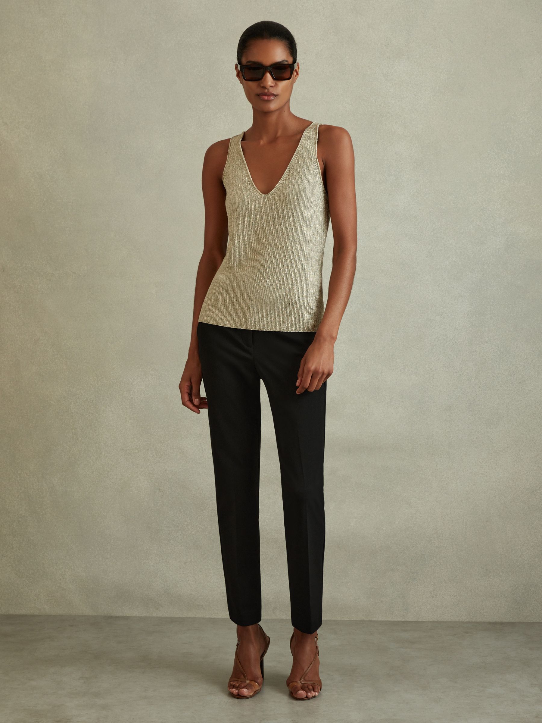 A woman wearing black slim fit tailored trousers with side and back pockets, a hook and zip fastening, and ankle length.
