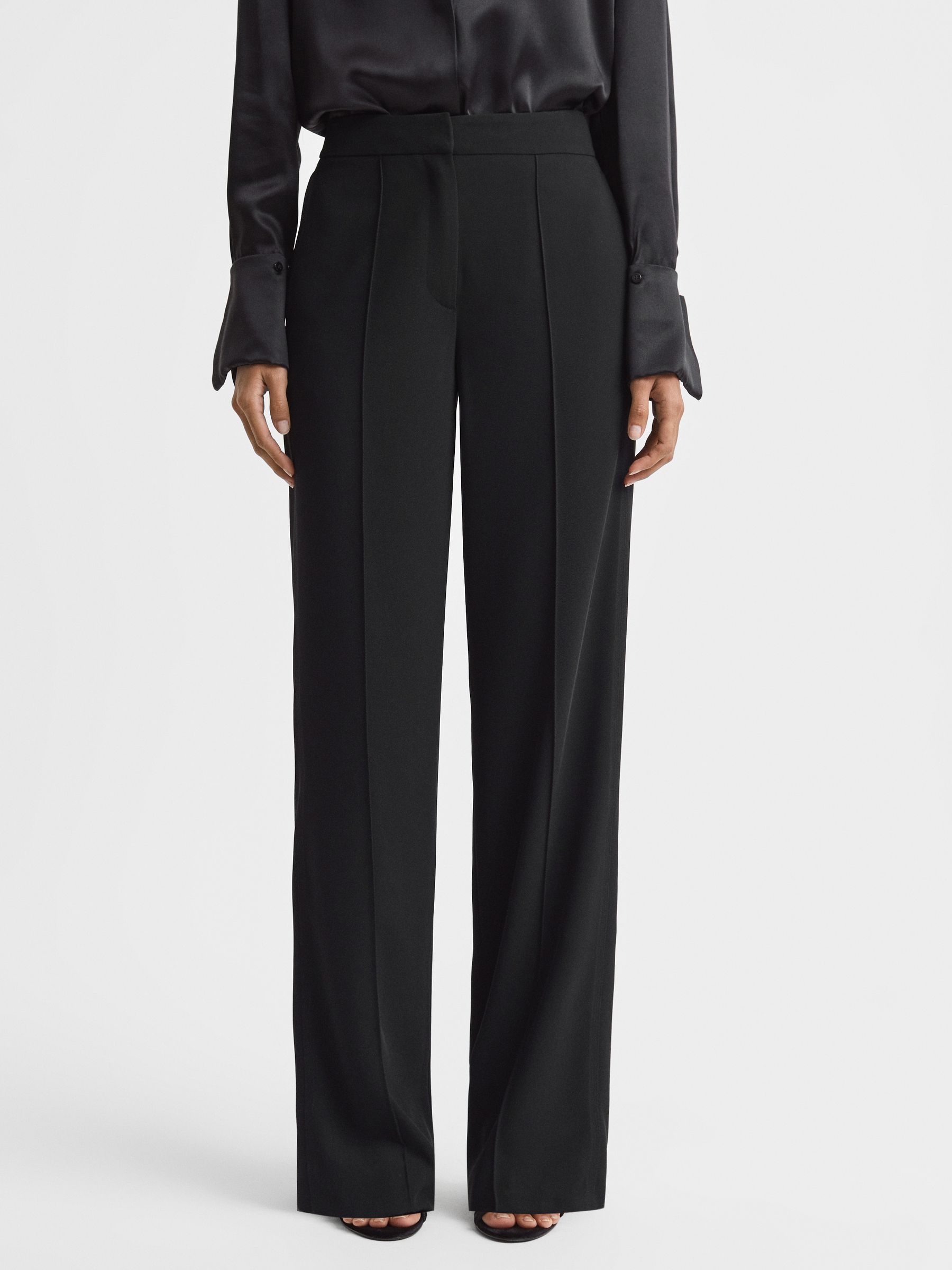 A pair of black women's trousers with a high waist, wide-leg cut, and side pockets, shown on a model.