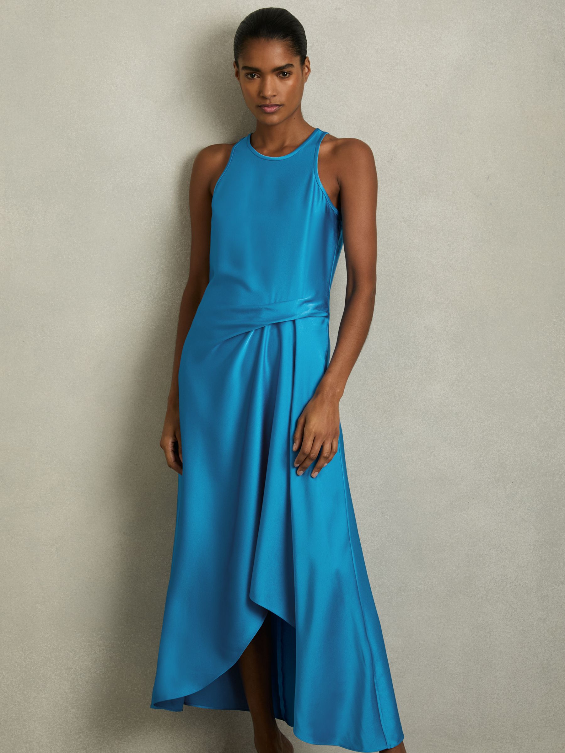 A woman wearing a blue satin midi dress with a draped tuck detail at the waist, keyhole back, and asymmetric hem.