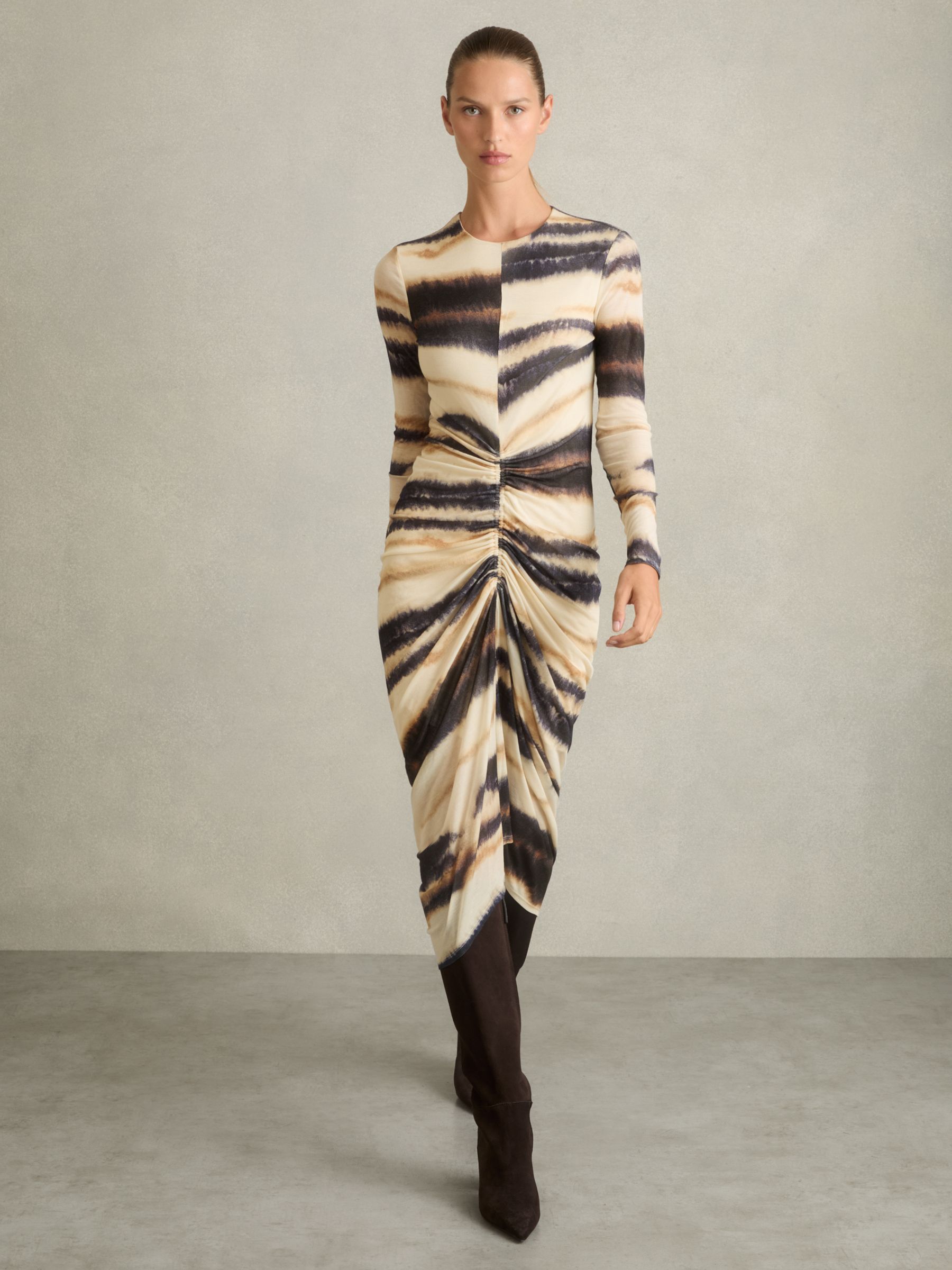 A woman wearing a long-sleeved, ruched dress with a graphic print in neutral and navy colors, featuring a crew neckline.