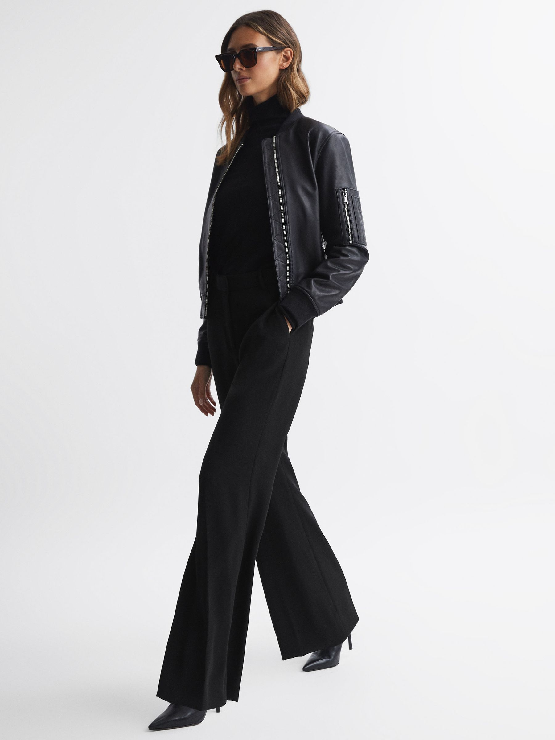 A pair of black petite wide-leg suit trousers with a mid-rise waist, belt loops, pressed creases, side slip pockets, and jetted pockets at the back.