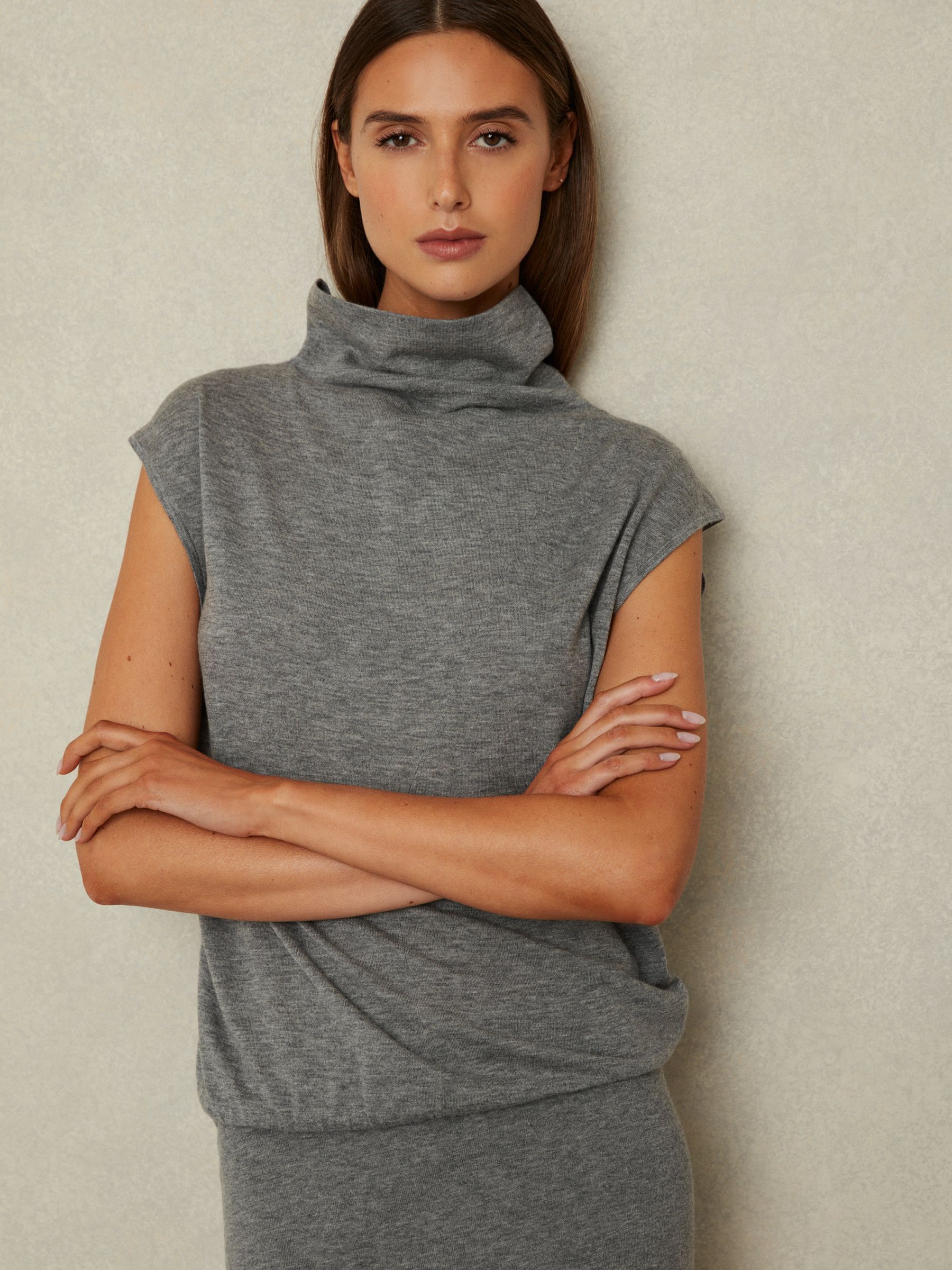 A woman wearing a grey knitted wool-cashmere midi dress with a funnel neckline and cap sleeves.