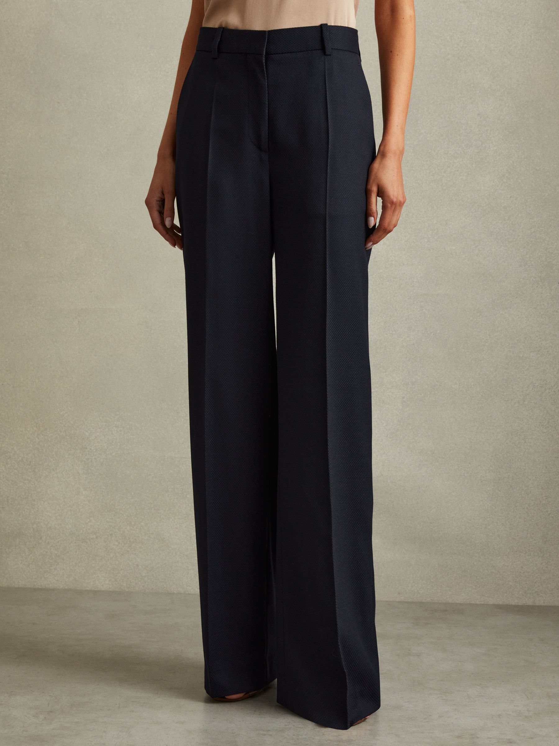A pair of navy textured wide-leg trousers with a mid-rise fit, pressed front creases, side pockets, and jetted pockets at the back, worn by a model.