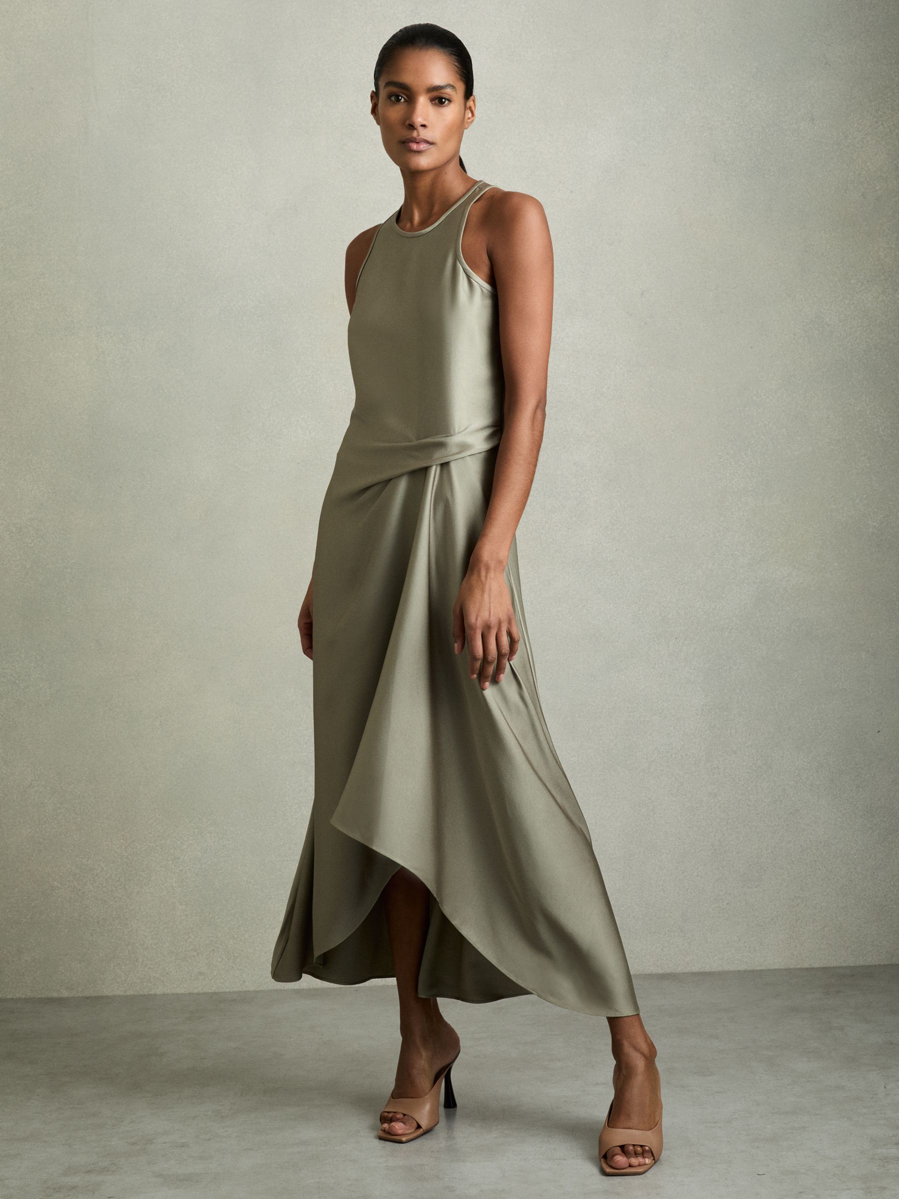 A woman wearing a khaki satin midi dress with a draped design, tuck detail at the waist, and asymmetric hemline.