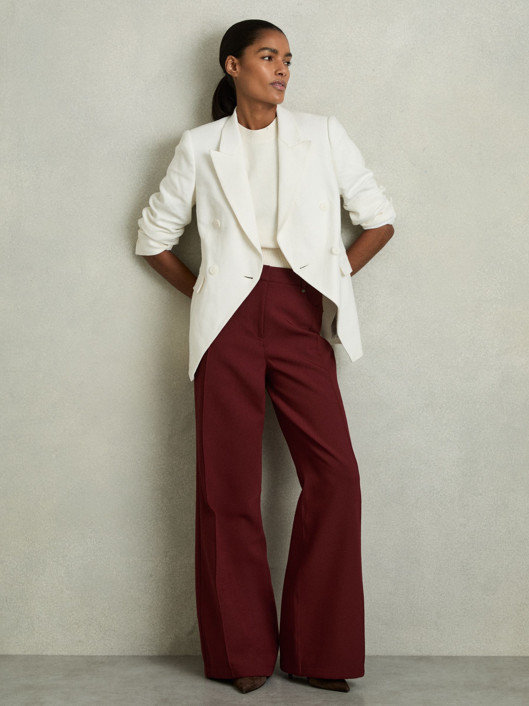A woman wearing dark red tailored palazzo trousers with a wide-leg silhouette, front pintucks, and pockets, paired with a white blazer and top.