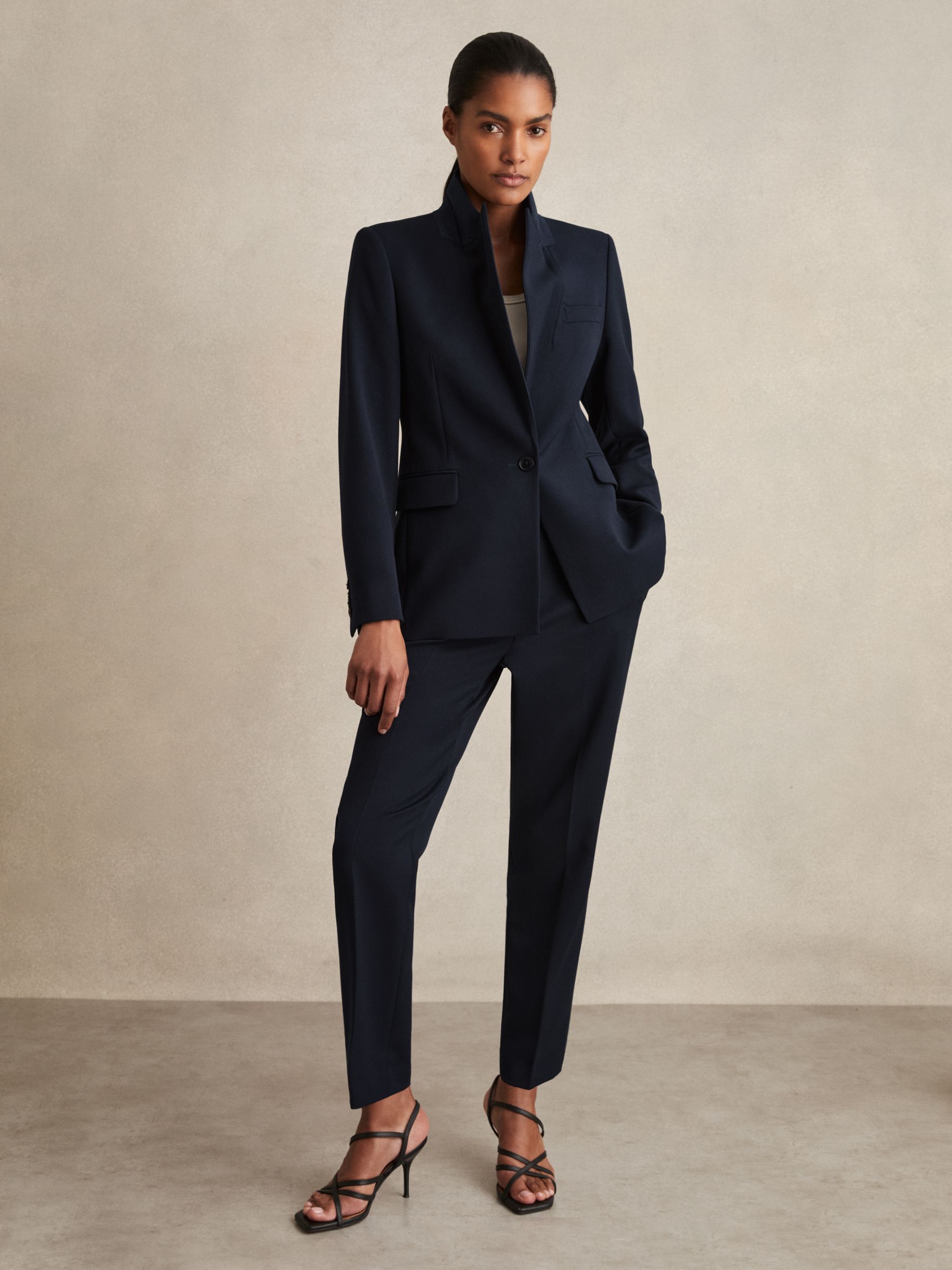 A pair of navy petite slim fit suit trousers with a mid-rise waist, belt loops, side-slip pockets, pressed creases, and a slim fit.