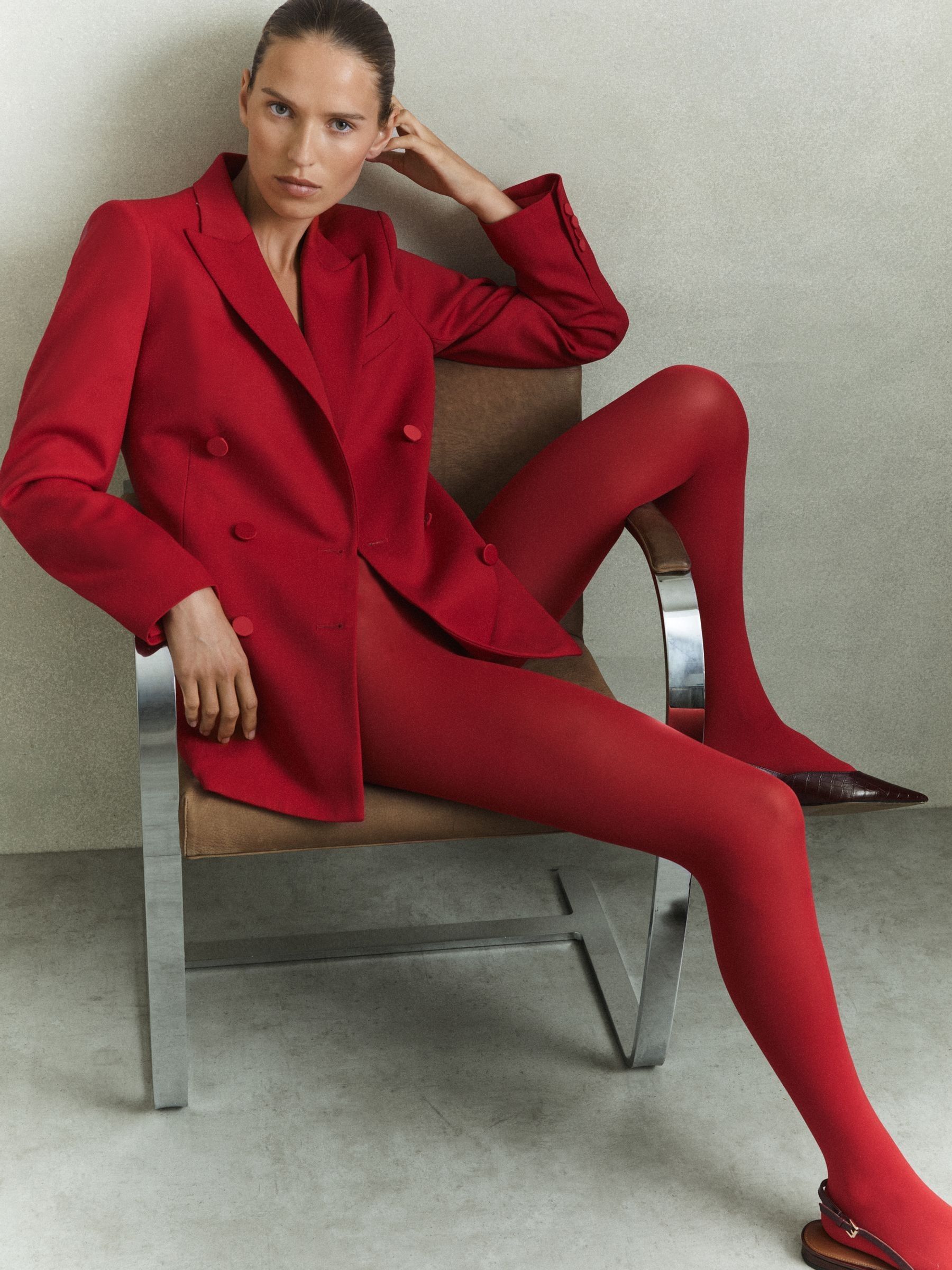 A woman wearing a red wool blend double-breasted tux blazer with satin details, matching trousers, and pointed shoes.