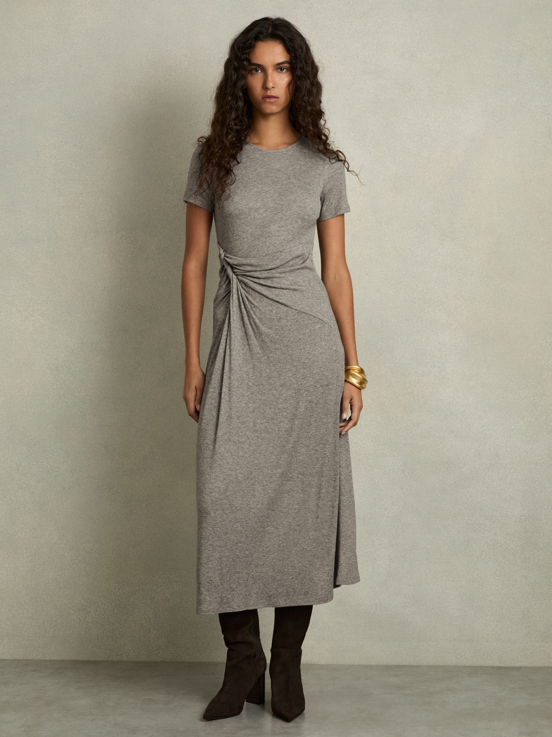 A woman wearing a grey midi dress with a twisted side detail, crew neck, and short sleeves.