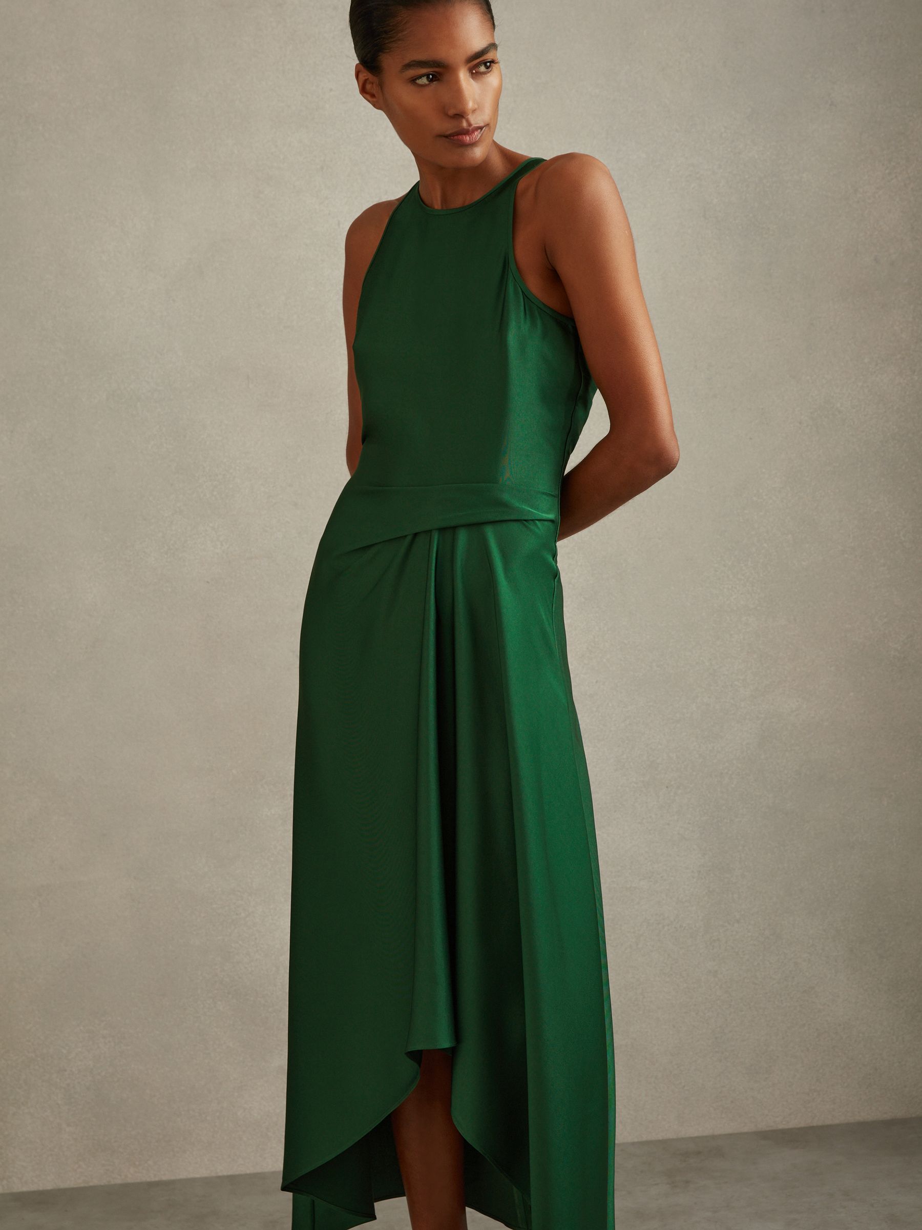 A woman wearing a green satin midi dress with a draped tuck detail at the waist, fitted silhouette, and keyhole back.