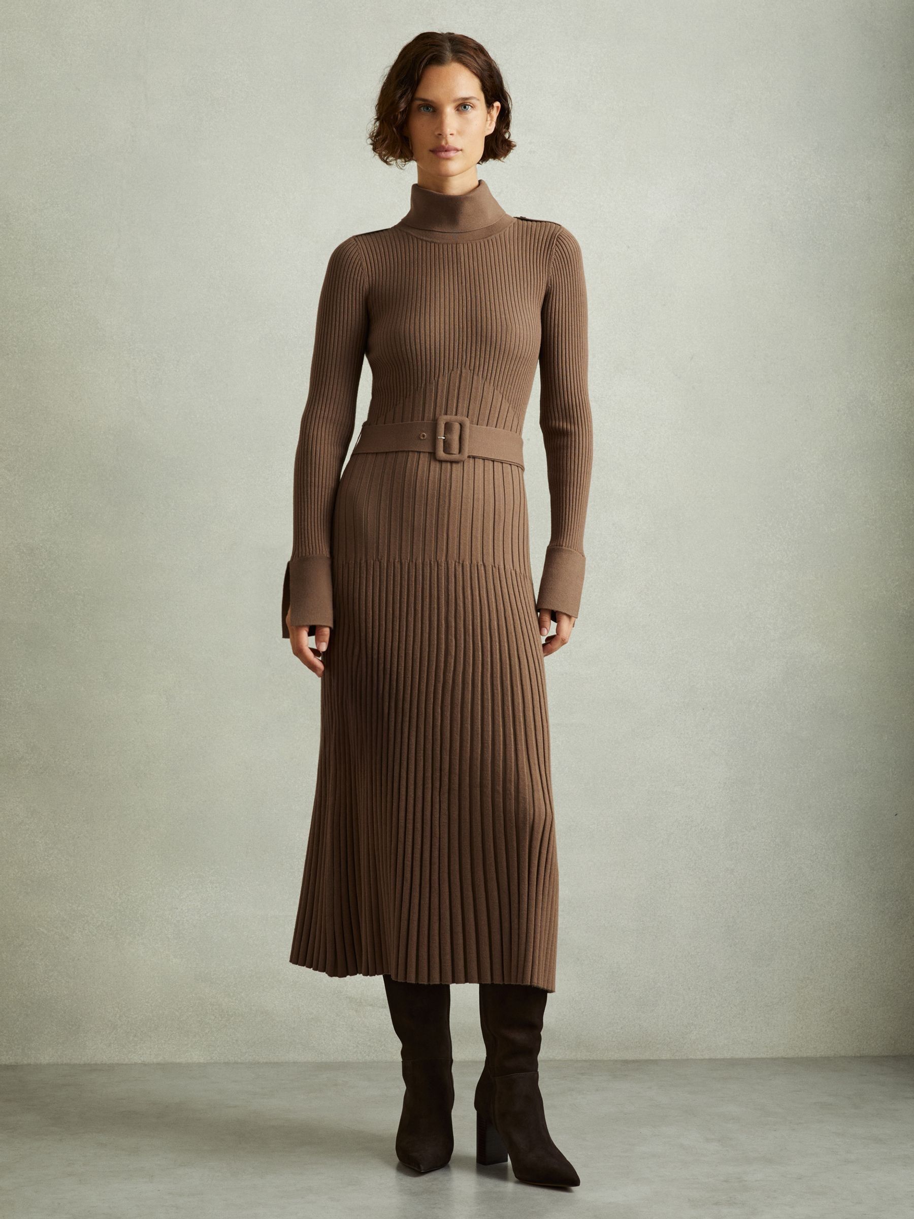 A woman wearing a Mocha-colored ribbed knit midi dress with a roll neckline, belted waist, epaulettes, and slit cuffs.