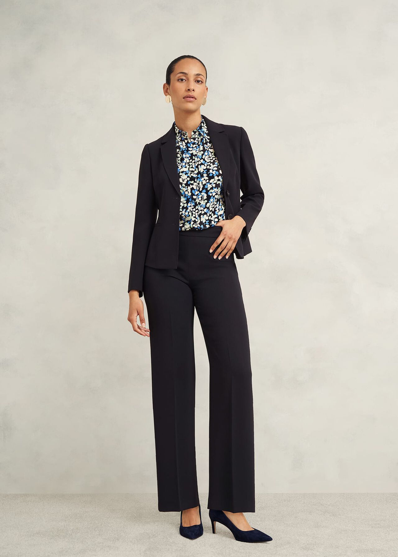 A woman wearing black wide-leg trousers with a side zip, paired with a patterned blouse and blazer.
