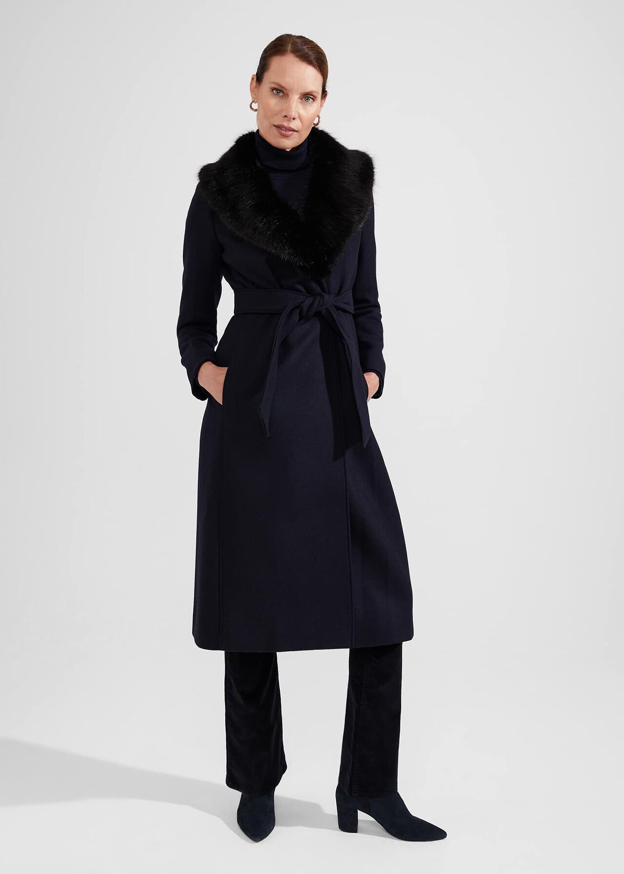 A woman wearing a navy blue wool blend coat with a collar, front fastening, and a black faux fur collar detail.
