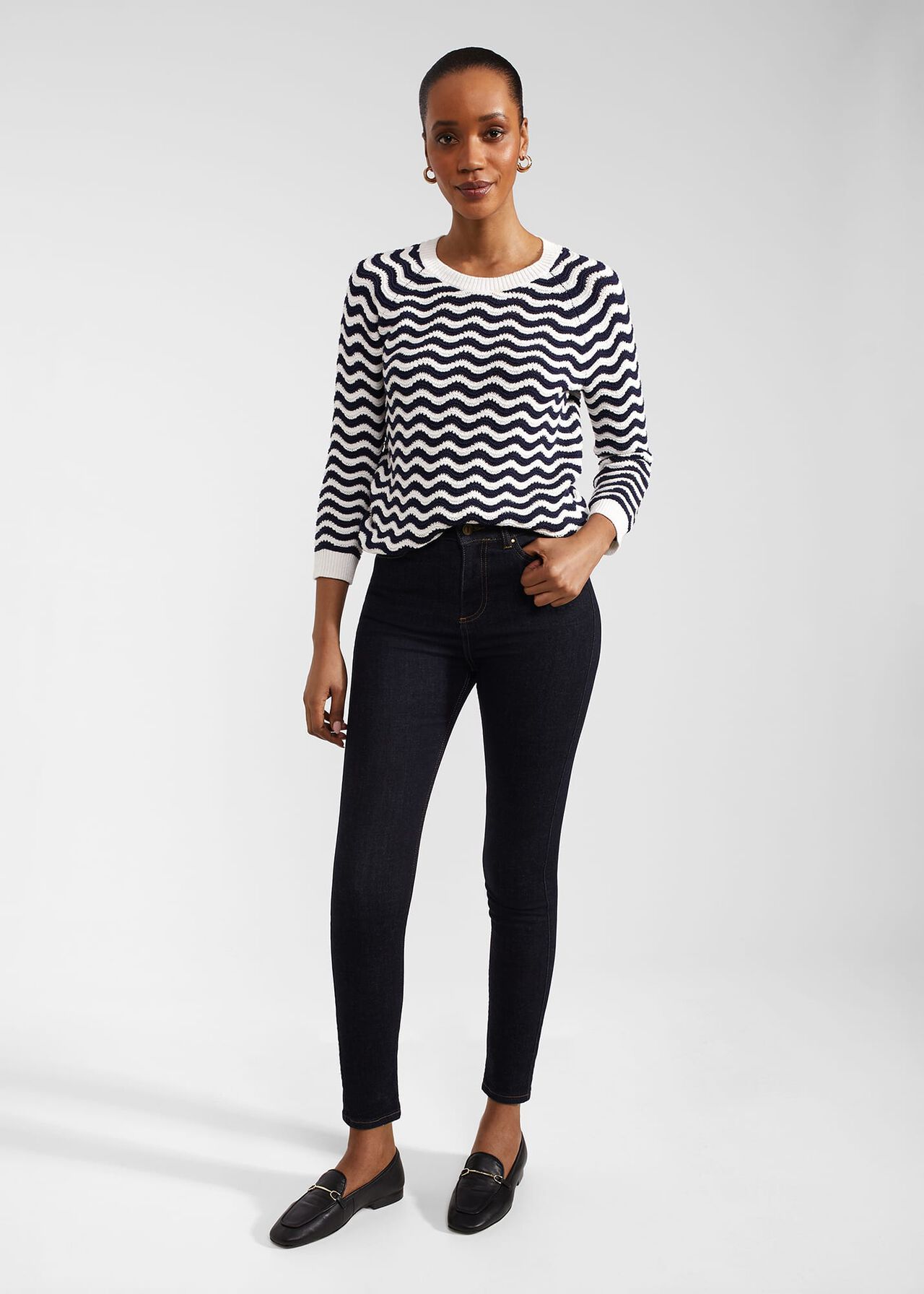 A woman wearing black Petite Gia Sculpting Jeans with a high waist and slim fit, paired with a striped sweater and loafers.