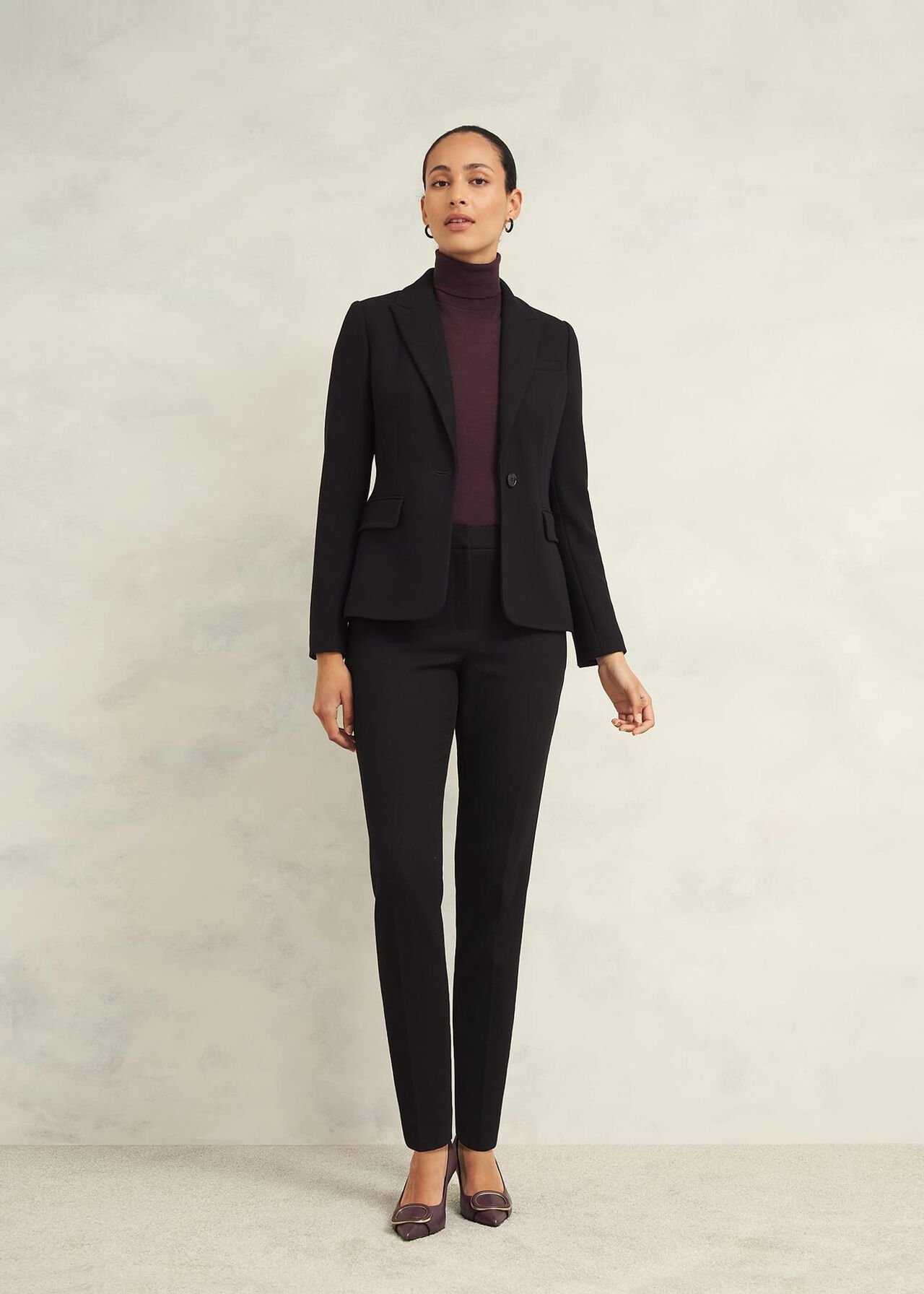 A pair of black petite slim trousers with a tailored fit, hook and bar fastening, and a model wearing them.