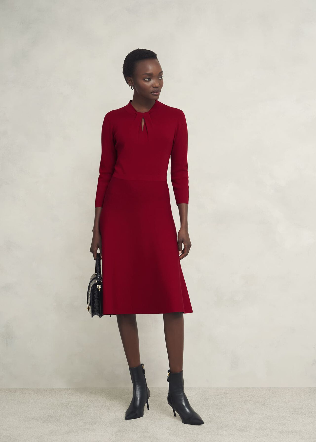 A woman wearing a red knitted dress with a notch neckline and long sleeves, standing against a plain background.