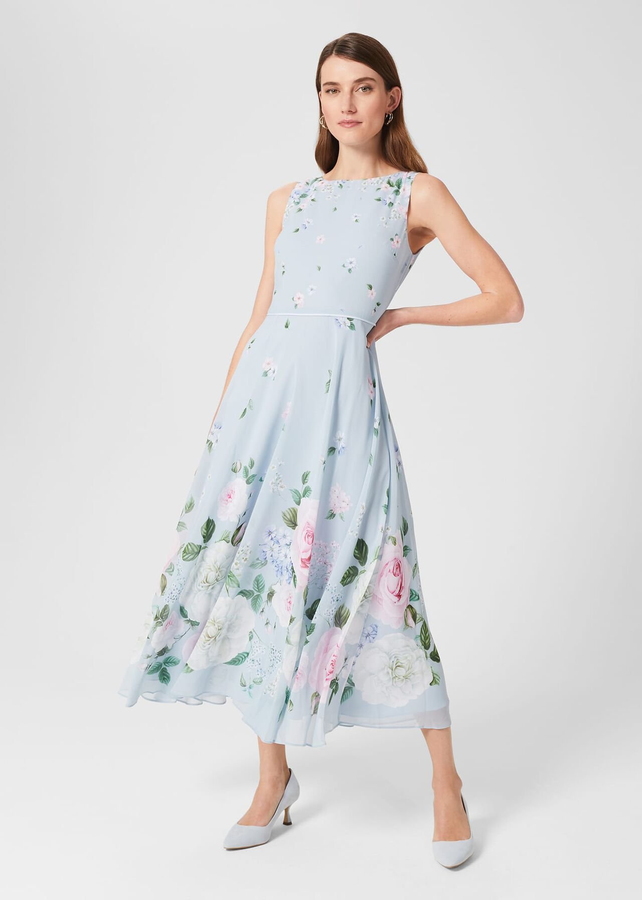 A woman wearing a light blue floral dress with a crew neckline, sleeveless, and a long flowing skirt with pastel floral patterns.