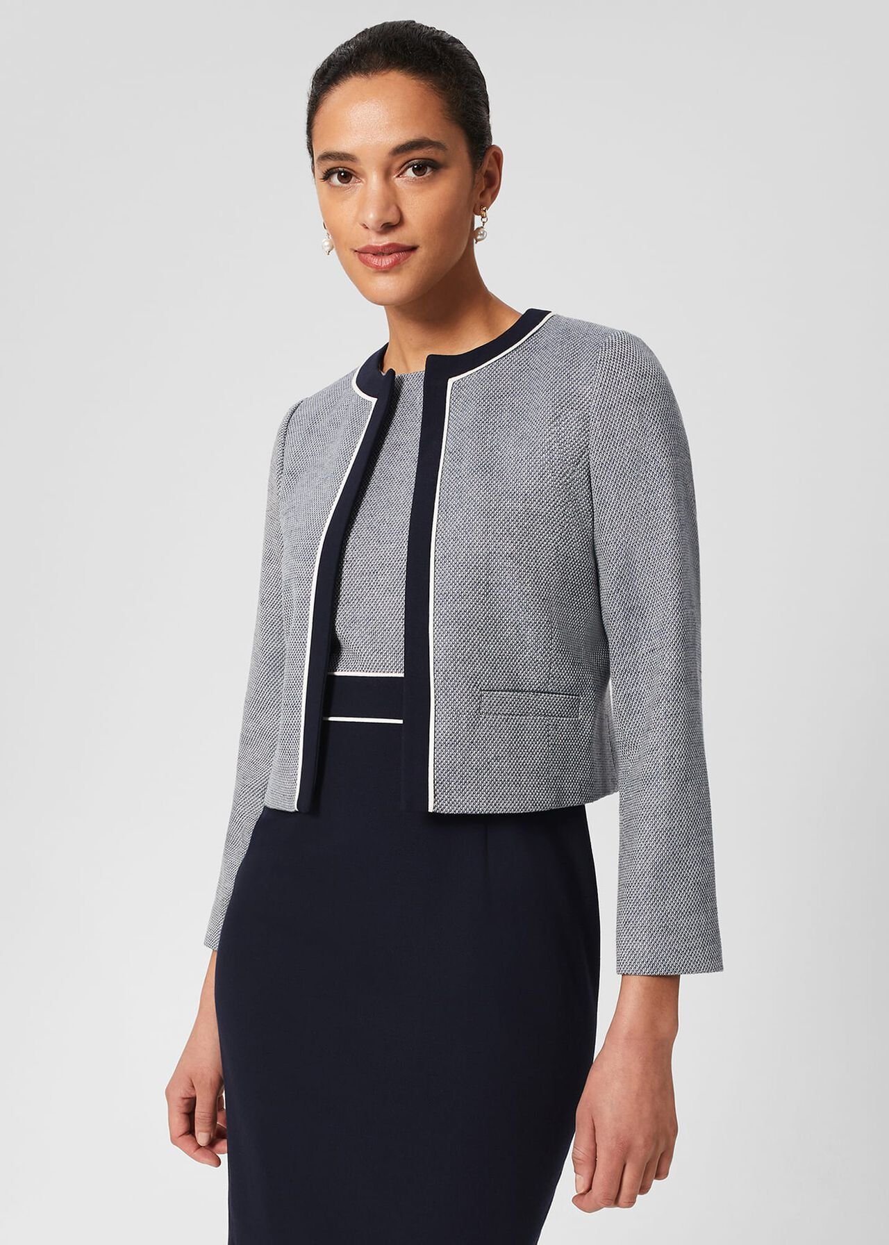 A woman wearing a light grey and navy petite Steph Jacket with a collar and single breast fastening, standing against a plain background.