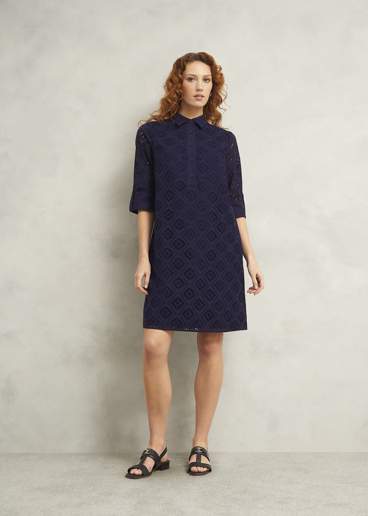 A woman wearing a navy blue broderie dress with a collar, three-quarter sleeves, and knee-length hem, standing against a plain background.