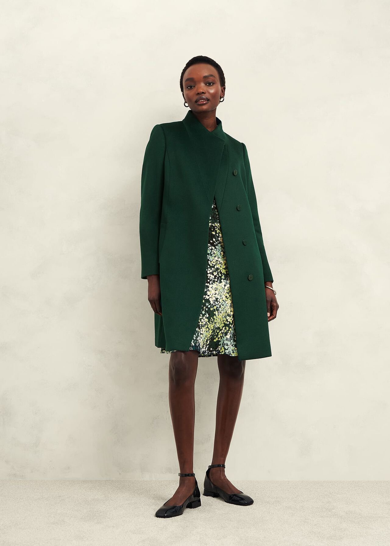 A woman wearing a green wool coat with a high neckline and front buttons, standing against a plain background.