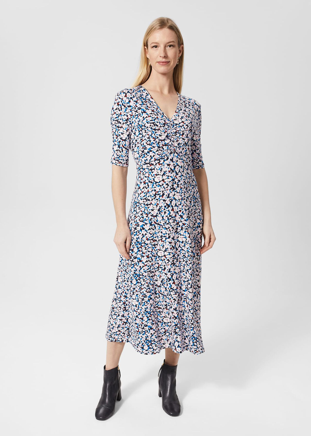 A woman wearing a multicolour floral midi dress with a V-neckline and three-quarter sleeves, paired with black ankle boots.