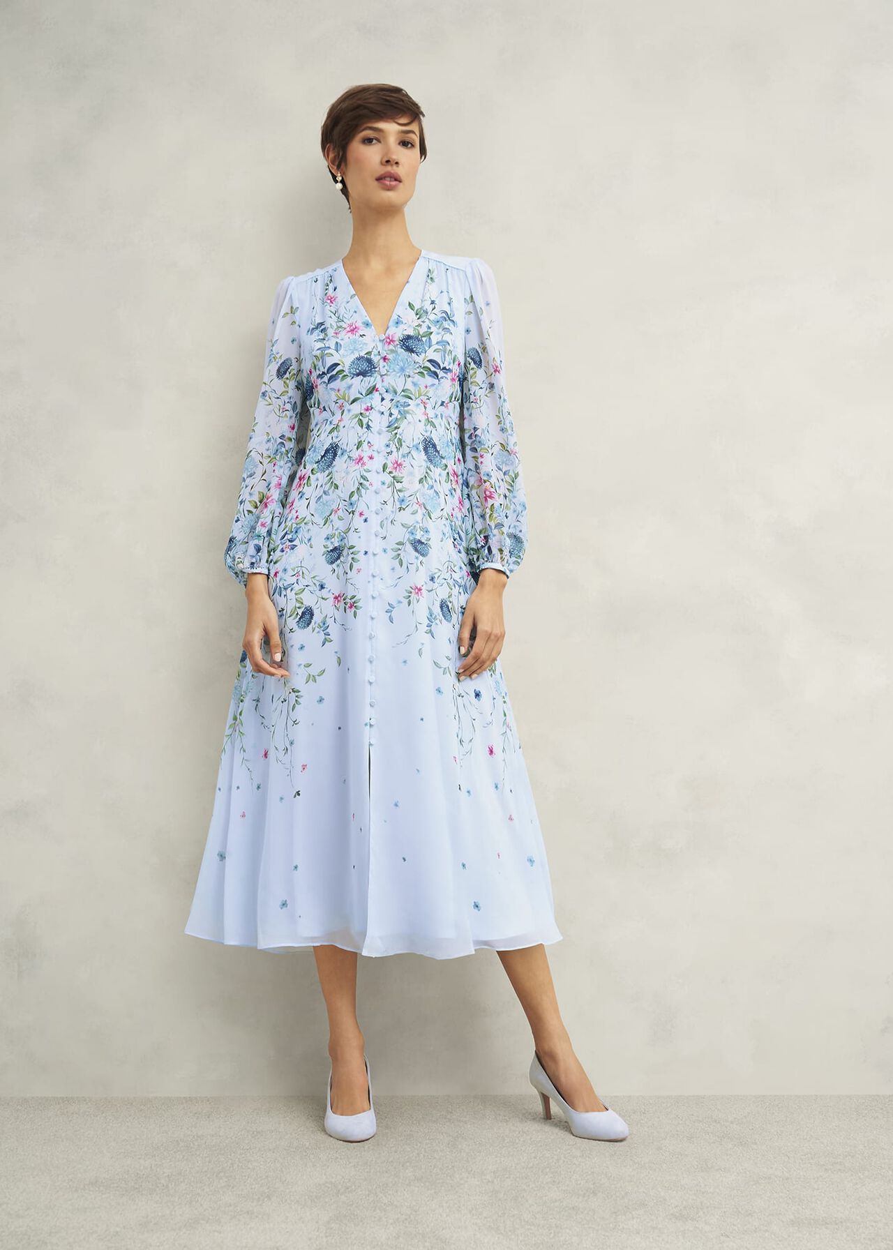 A woman wearing a white floral silk dress with long sleeves, V-neckline, and a midi length, featuring a multicolour floral pattern.