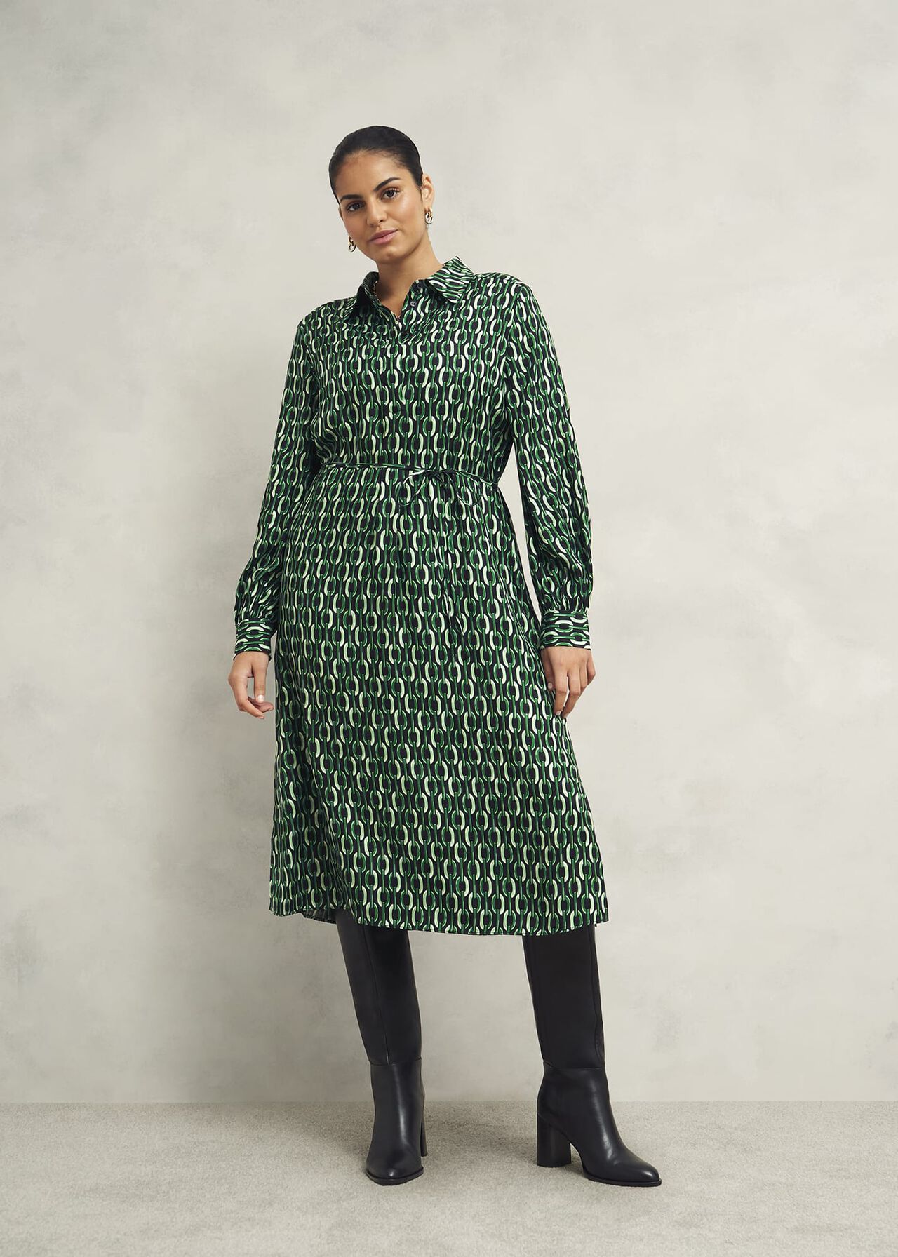 A woman wearing a green and black geometric patterned midi dress with a collar, long sleeves, and a side zip, paired with black knee-high boots.