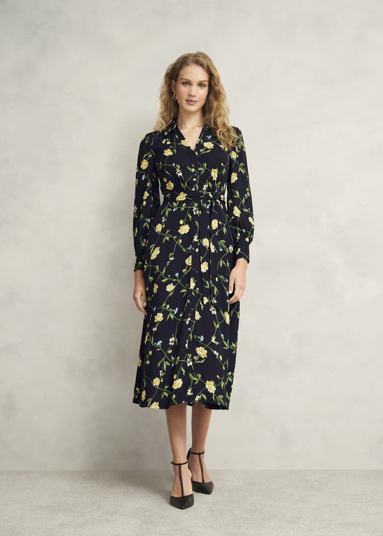 A woman wearing a navy floral midi dress with long sleeves, a collar, and a front fastening.