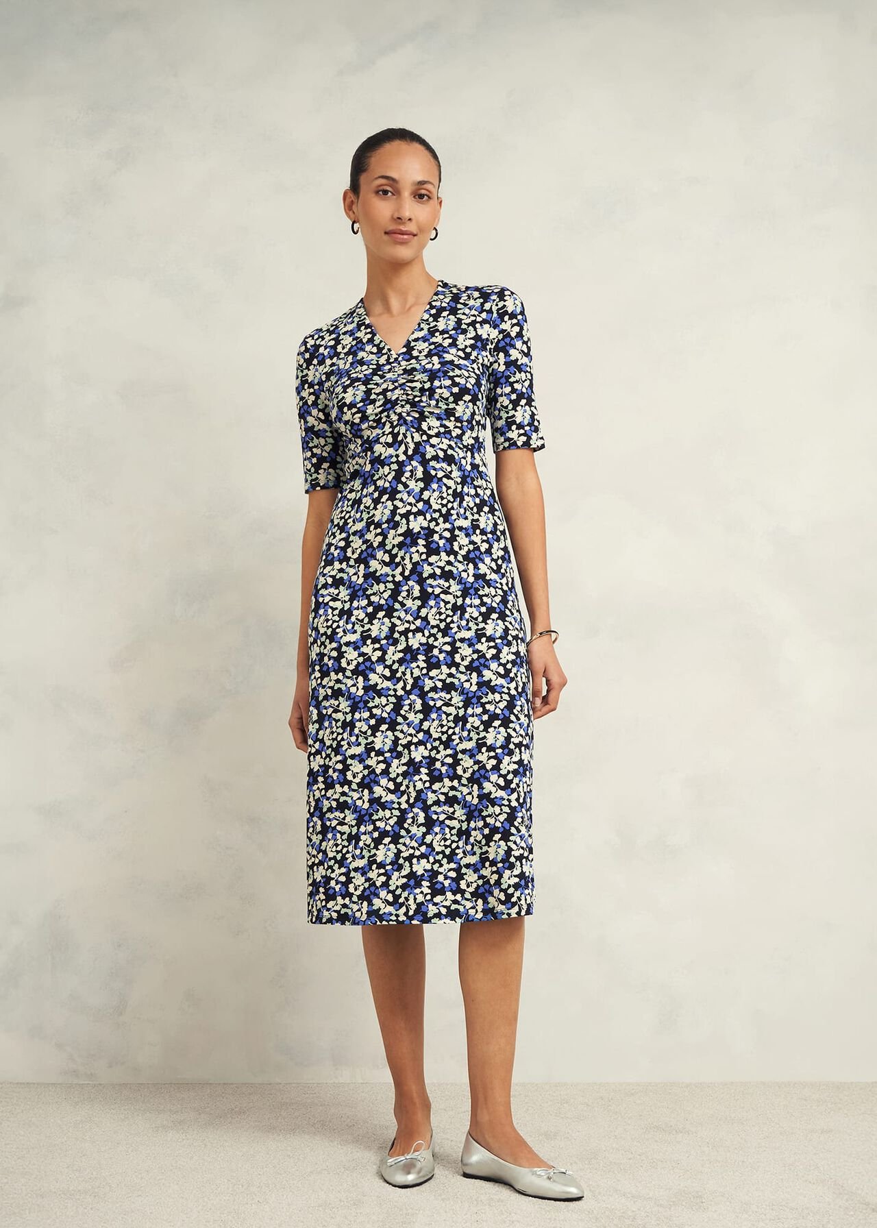 A woman wearing a blue floral midi dress with a V-neckline and short sleeves, standing against a plain background.