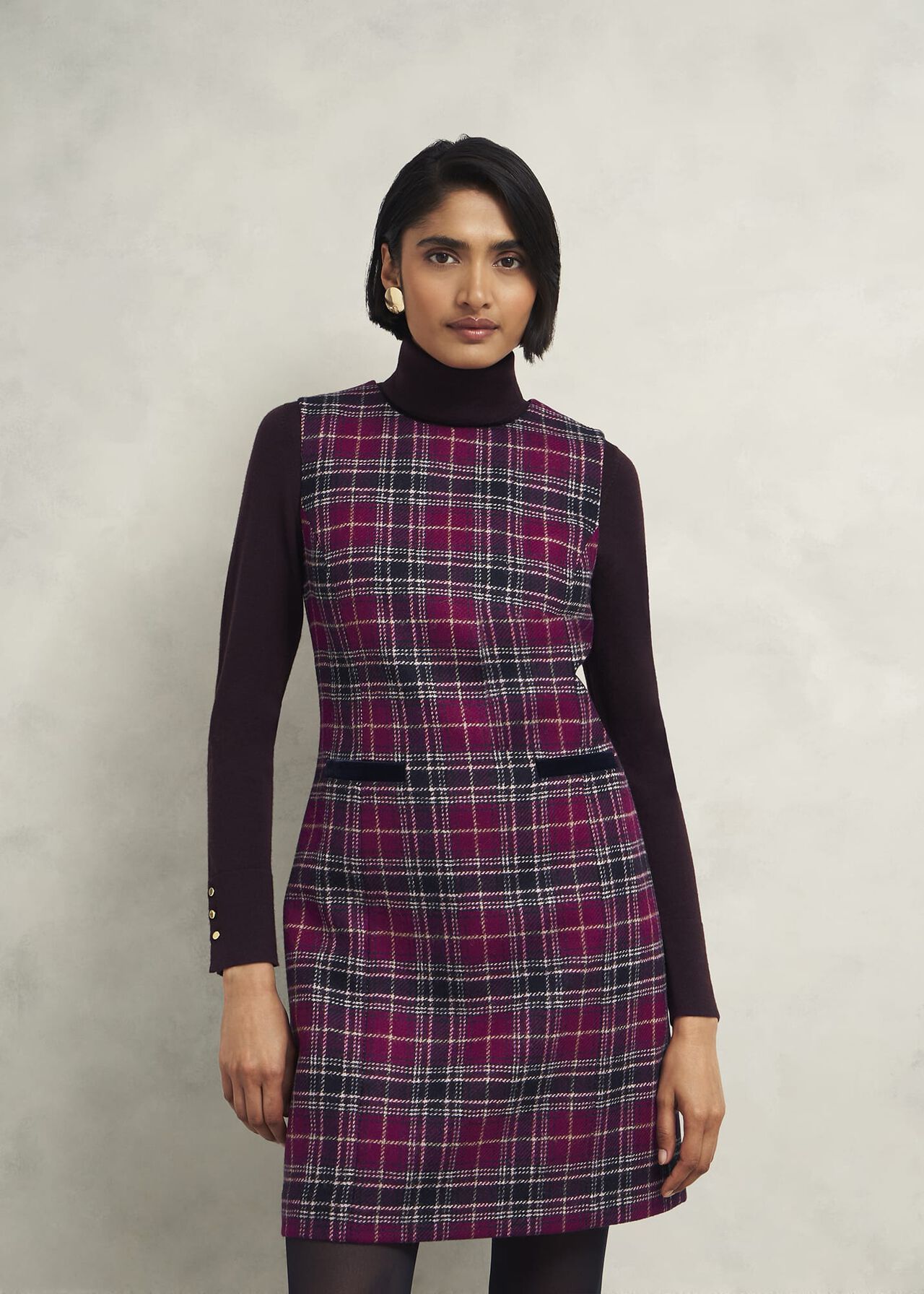 A woman wearing a plaid wool dress with long sleeves, crew neckline, and a fitted silhouette, in shades of red, black, and white.