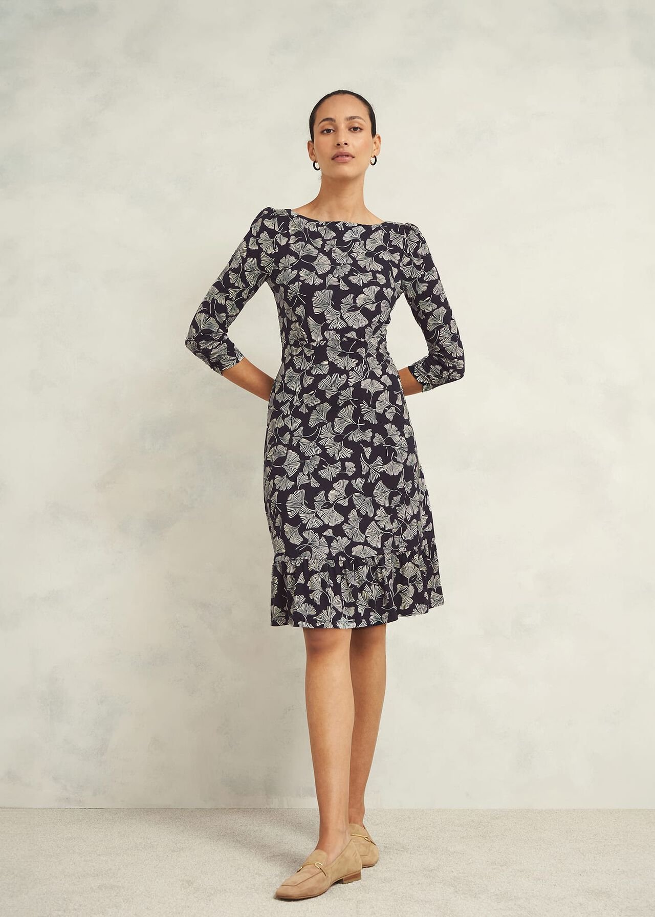 A woman wearing a black knee-length dress with a white ginkgo leaf print, boat neckline, and three-quarter sleeves, standing against a plain background.