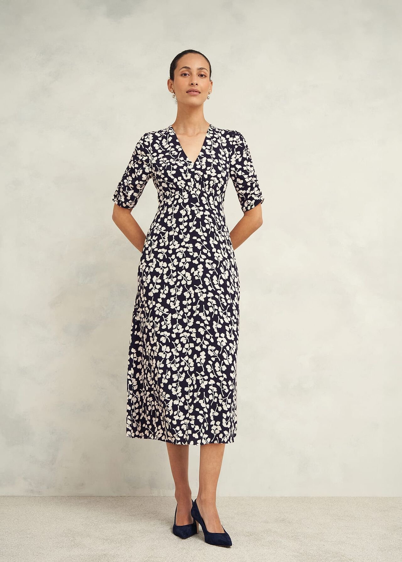 A woman wearing a navy and white floral midi dress with a V-neckline and three-quarter sleeves, standing against a plain background.